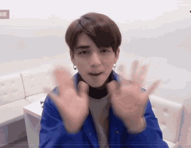 a young man in a blue jacket is waving his hands in front of a white couch