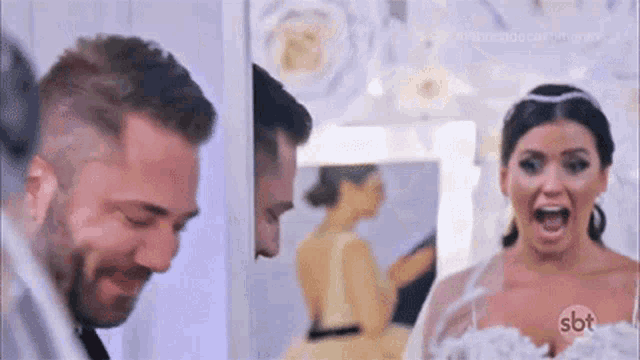 a man and a woman are standing next to each other in front of a mirror . the woman is wearing a wedding dress .