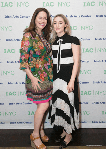 two women posing for a picture in front of a wall that says irish arts center