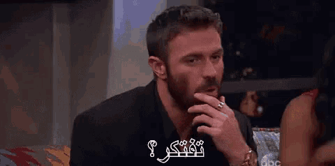 a man with a beard and a ring on his finger is sitting in front of a woman .
