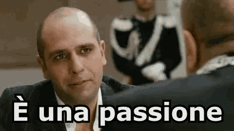 a bald man in a suit and tie is talking to another man in front of a group of people .