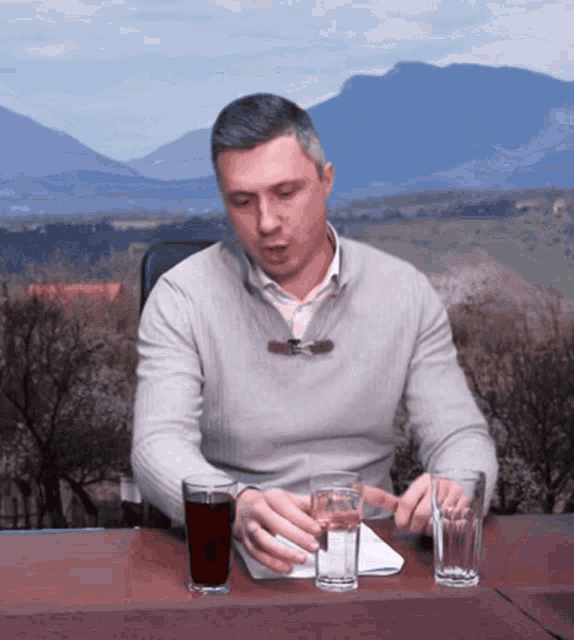 a man is sitting at a table with two glasses of liquid on it