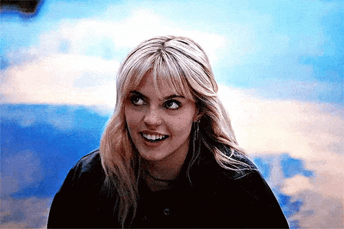 a woman with blonde hair and bangs is smiling and looking at the camera .