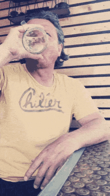 a man wearing a yellow shirt that says pilier drinking from a glass