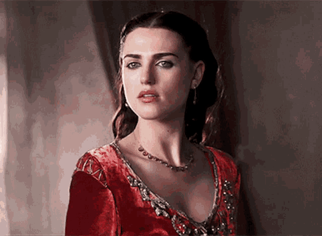a woman wearing a red dress and a necklace is looking at the camera .