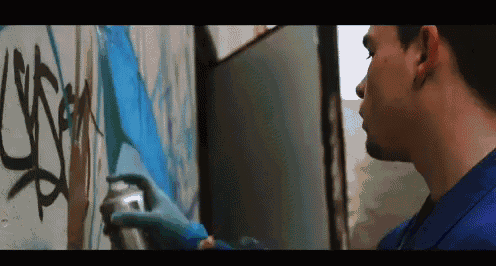 a man wearing blue gloves is spray painting graffiti on a wall with a spray can