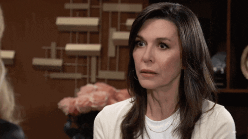 a woman in a white shirt looks at the camera with a serious look on her face