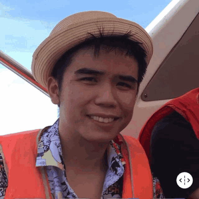 a young man wearing a straw hat and an orange vest