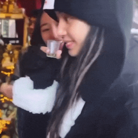 a woman is drinking from a shot glass while another woman holds a can of soda .