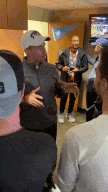 a group of men are standing in a room talking to each other . one of the men is wearing a nike hat .