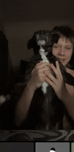 a boy holds a black and white dog in his hands