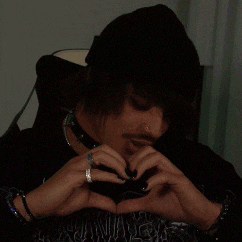 a man wearing a black hat and a choker is making a heart shape