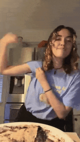 a girl in a blue shirt is flexing her arm in front of a plate of food .