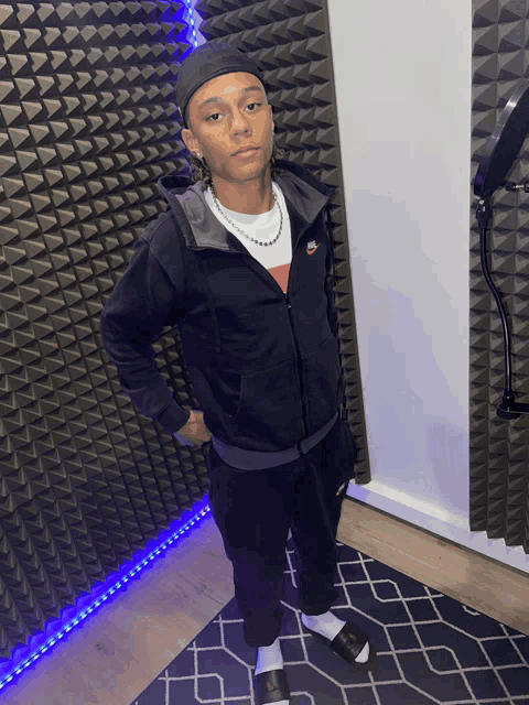 a man wearing a black nike hoodie stands in front of a wall with triangles on it