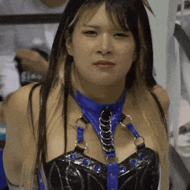 a woman wearing a blue and black outfit with rings around her neck looks at the camera