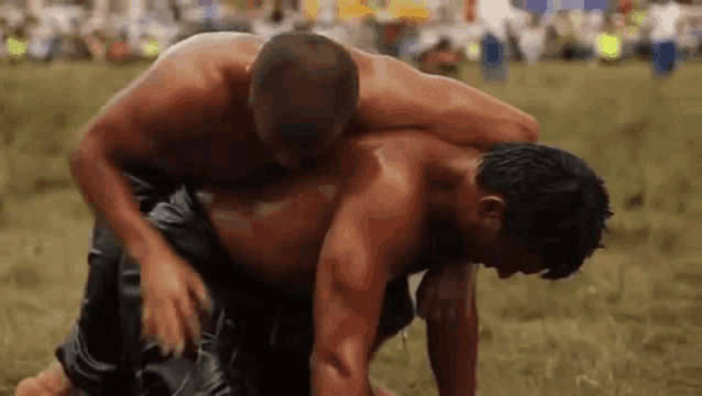 two men are wrestling in a field and one of them is carrying the other on his back .