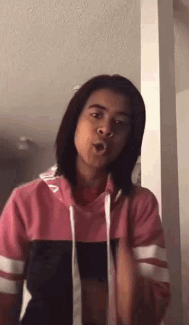 a woman in a pink hoodie is making a funny face .