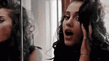 a woman is looking at herself in a mirror and making a surprised face .