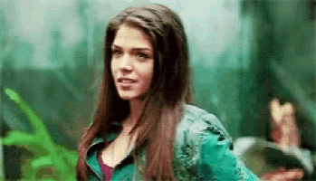a woman with long hair is wearing a green jacket and standing in front of a green background .