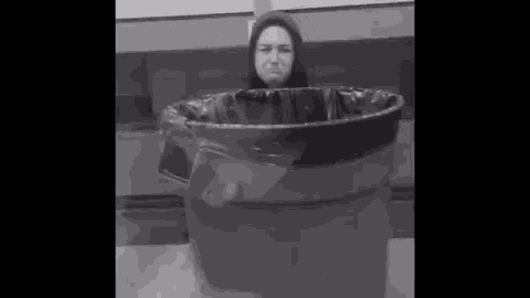 a woman is standing in a trash can with her head sticking out of it .