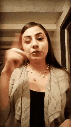a woman wearing a cardigan and a necklace is standing in a hallway .