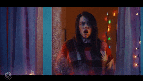 a woman is standing in front of a window with her mouth open and christmas lights behind her .