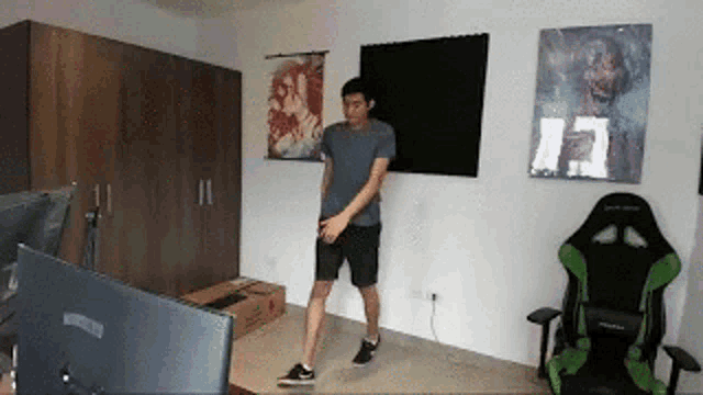 a man is standing in a room with a green chair and a computer monitor