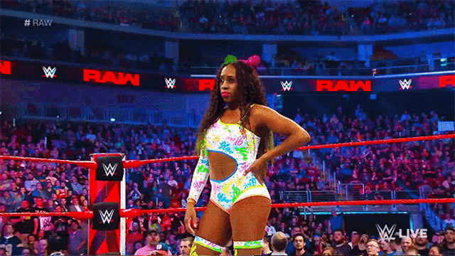 a female wrestler is standing in a wrestling ring with a crowd in the background .