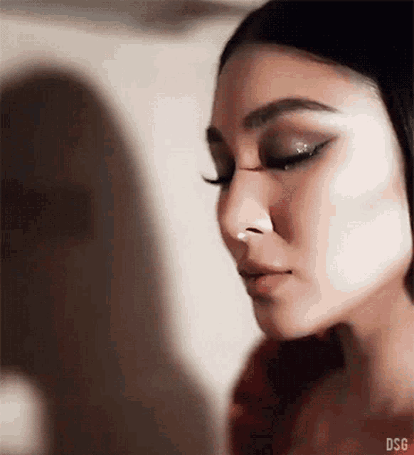 a close up of a woman 's face with a nose ring and a shadow behind her that says dsg