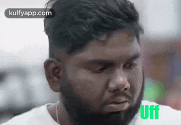 a man with a beard and a white shirt is making a sad face .