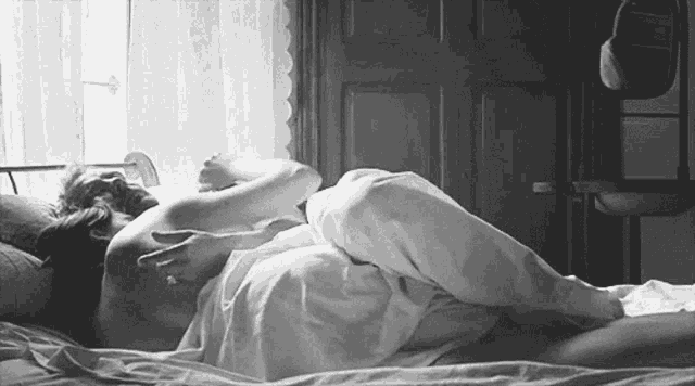 a black and white photo of a man and a woman laying in bed .