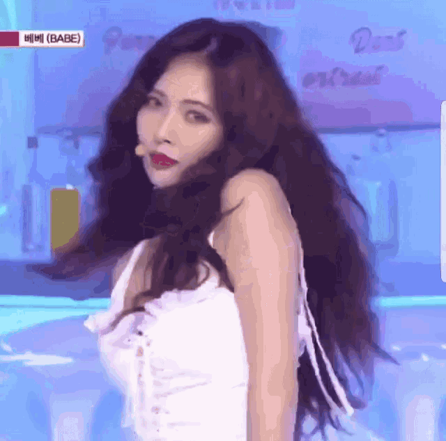 a woman with long dark hair is wearing a white top and a red lip .