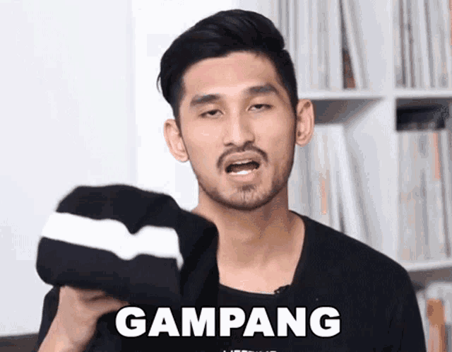 a man with a beard is holding a black shirt that says gampang on it