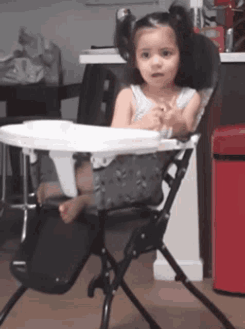 a little girl is sitting in a high chair with a tray on it