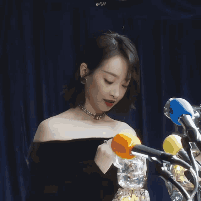 a woman in a black off the shoulder top is standing in front of a row of microphones