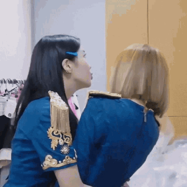 two women are kissing each other in a room . one of the women is wearing a blue dress .