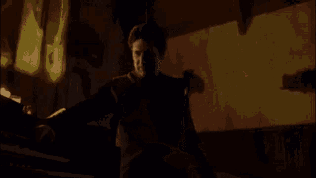 a man is playing a piano in a dark room with a yellow light behind him .
