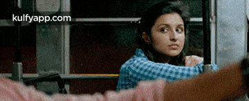 a woman in a blue plaid shirt is sitting on a bus looking out the window .
