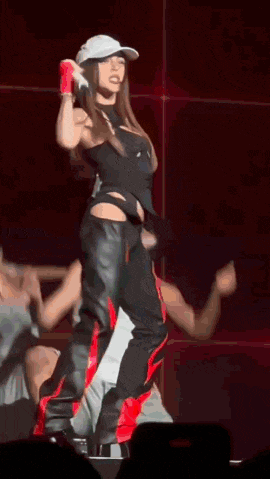 a woman is standing on a stage wearing a hat and gloves while holding a microphone .