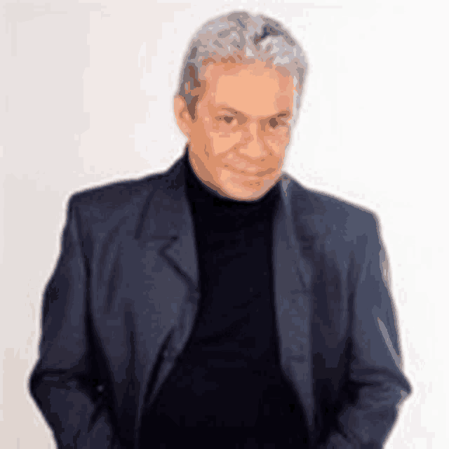 a man wearing a suit and a black turtleneck is smiling .