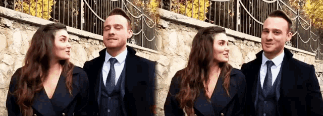 a man and woman are standing next to each other in front of a stone wall