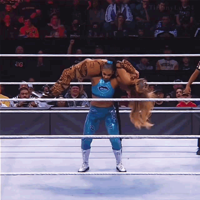 a wrestler in a blue outfit is carrying another wrestler on her back