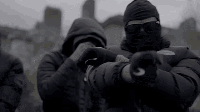 a man wearing a mask and sunglasses is pointing at another man .