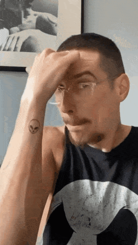 a man wearing glasses has an alien tattoo on his arm