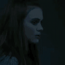 a woman in a dark room looking out a window