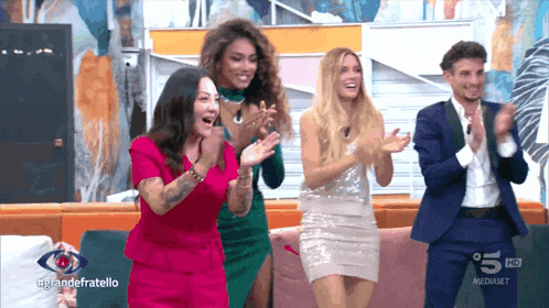 a group of people are applauding in front of a sign that says #grandefratello on it