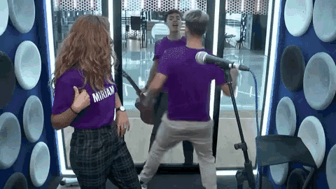 a woman in a purple shirt with the word miriam on it is dancing in front of a microphone