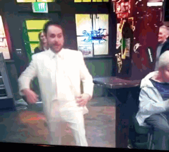 a man in a white suit dancing in front of a green exit sign