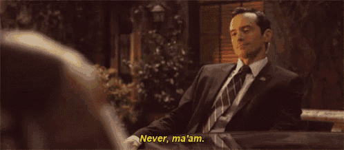 a man in a suit and tie is sitting at a table and talking to someone .