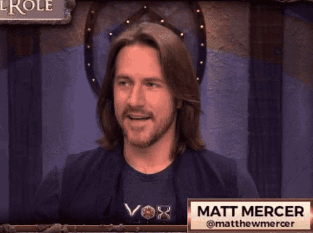 a man with long hair is sitting at a table with a name tag that says matt mercer